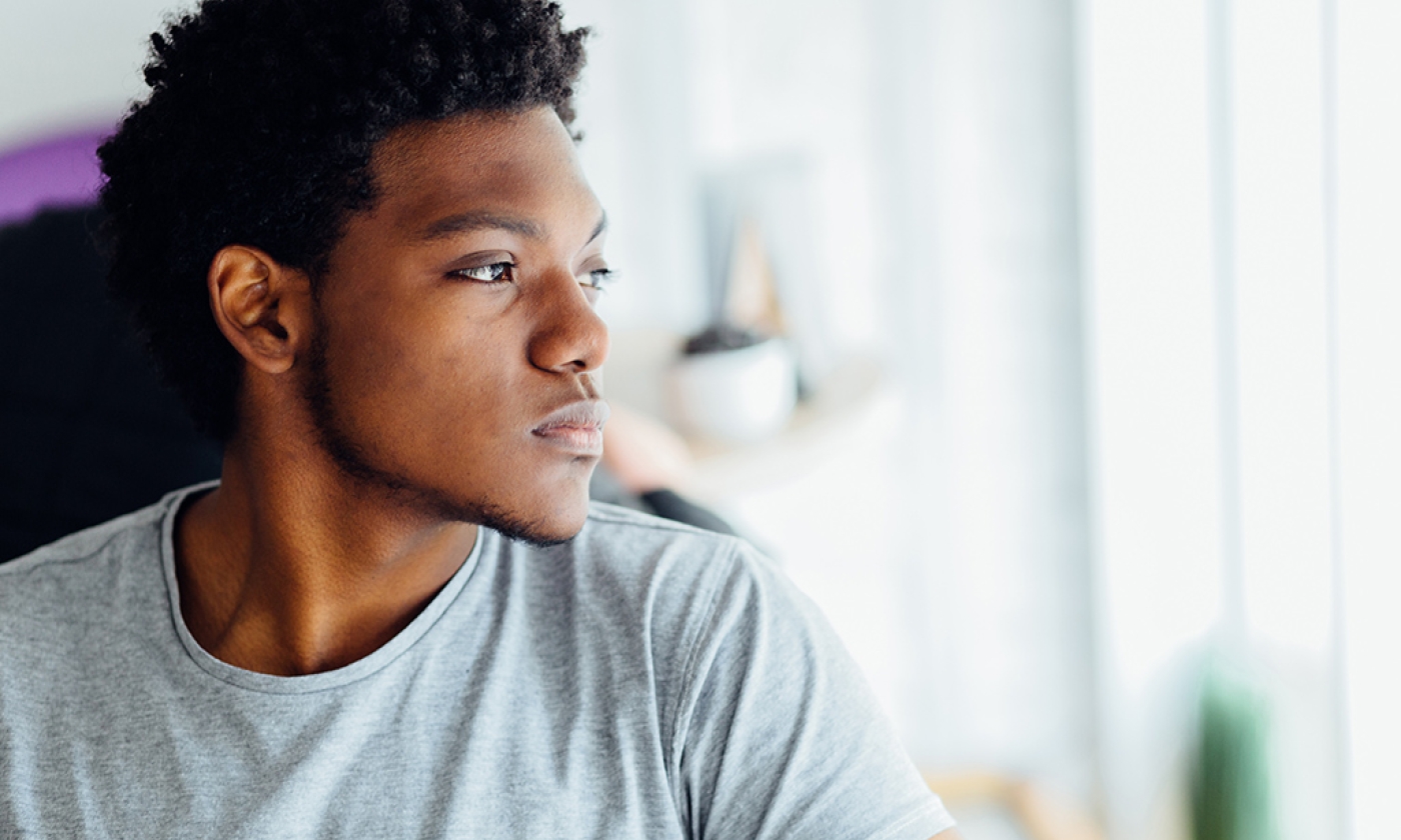 Headshot portrait of young man looking aside and appearing isolated in front of a blurred indoors background.